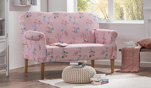 Die perfekte Größe: Ein rosa Küchensofa mit floralem Muster steht an einem Fenster. Davor ein kleiner Couchtisch in hellrosa.