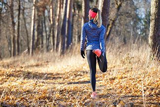 Langarmshirts für die richtige Temperatur: Eine junge Frau dehnt ihre Beine vor dem Joggen, während sie in einem herbstlichen Wald steht.