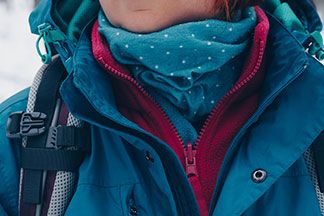 Lagenlook mit Fleece: Nahaufnahme einer Wanderin mit Rucksack und Schal, die unter einer blauen Allwetterjacke eine pinke Fleecejacke trägt.