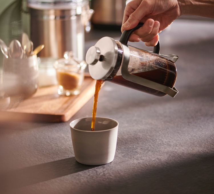Kaffee wird aus einer Siebstempelkanne in eine Kaffeetasse gegossen