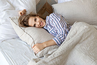 Eine Frau liegt im Bett und trägt einen blau weiß gestreiften Schlafanzug.