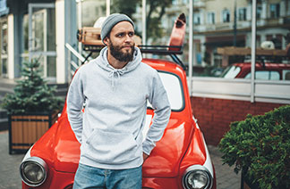 Ein Mann in einem grauen Kapuzenpullover lehnt vor einem Auto.