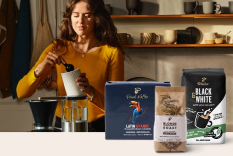 Eine Frau löffelt gemahlenen Filterkaffee aus einer Dose, daneben sind der Latin Grande, Black and White und Blonde Roast präsentiert.