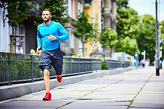 Die richtige Herrenhose für den Sport: Ein bärtiger Mann mit Langarmshirt und Sporthose joggt durch eine Stadt.