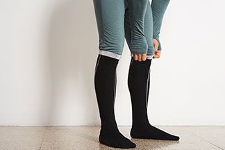 Funktionswäsche richtig tragen: Nahaufnahme eines Mannes, der sich über seine Thermo-Skiunterwäsche seine Thermosocken zieht.