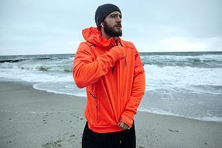 Ein Mann steht mit seiner orangen Sportjacke am Strand.