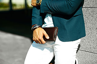 Stylischer Mann mit Accessoires steht angelehnt an der Wand.
