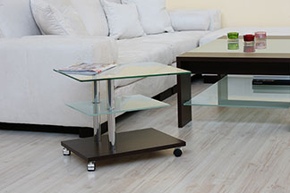 Bei Tchibo erhalten Sie qualitativ hochwertige Beistelltische: Ein Wohnzimmer mit einer weißen Couch und einem rechteckigen Beistelltisch aus Glas, der auf Rollen steht.