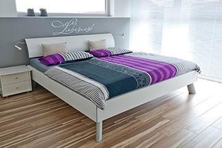 Ein gemachtes Bett mit lilafarbener Bettwäsche steht im Schlafzimmer.