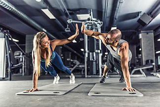 Fitness-Zubehör in Top-Qualität: Eine junge Frau und ein junger Mann trainieren auf jeweils einer Sportmatte und klatschen sich gegenseitig ab.