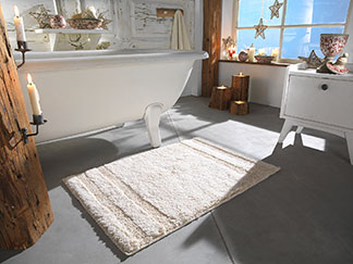 Die richtige Form finden: Ein rechteckiger weißer Badteppich liegt vor einer freistehenden Badewanne im Badezimmer.