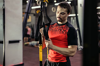 Ein sportlicher Mann in einem farbigen Sport-T-Shirt stellt sich ein Sportgerätes in einem Fitnessstudio ein.