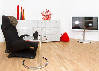 Beistelltische sind nicht nur praktisch: Ein Wohnzimmer mit einem weißen Sideboard, einem schwarzen Sessel, einem Fernseher und einem runden Beistelltisch.