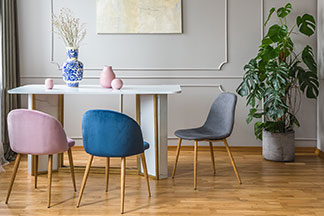 Stylische Form: An einem rechteckigen, weißen Tisch stehen drei schalenförmige Esszimmerstühle ohne Armlehnen in pink, blau und grau.