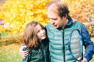 Herrenwesten für Klein und Groß: Vater und Sohn stehen Arm in Arm mit einem Tennisschläger in der Hand in der Natur.
