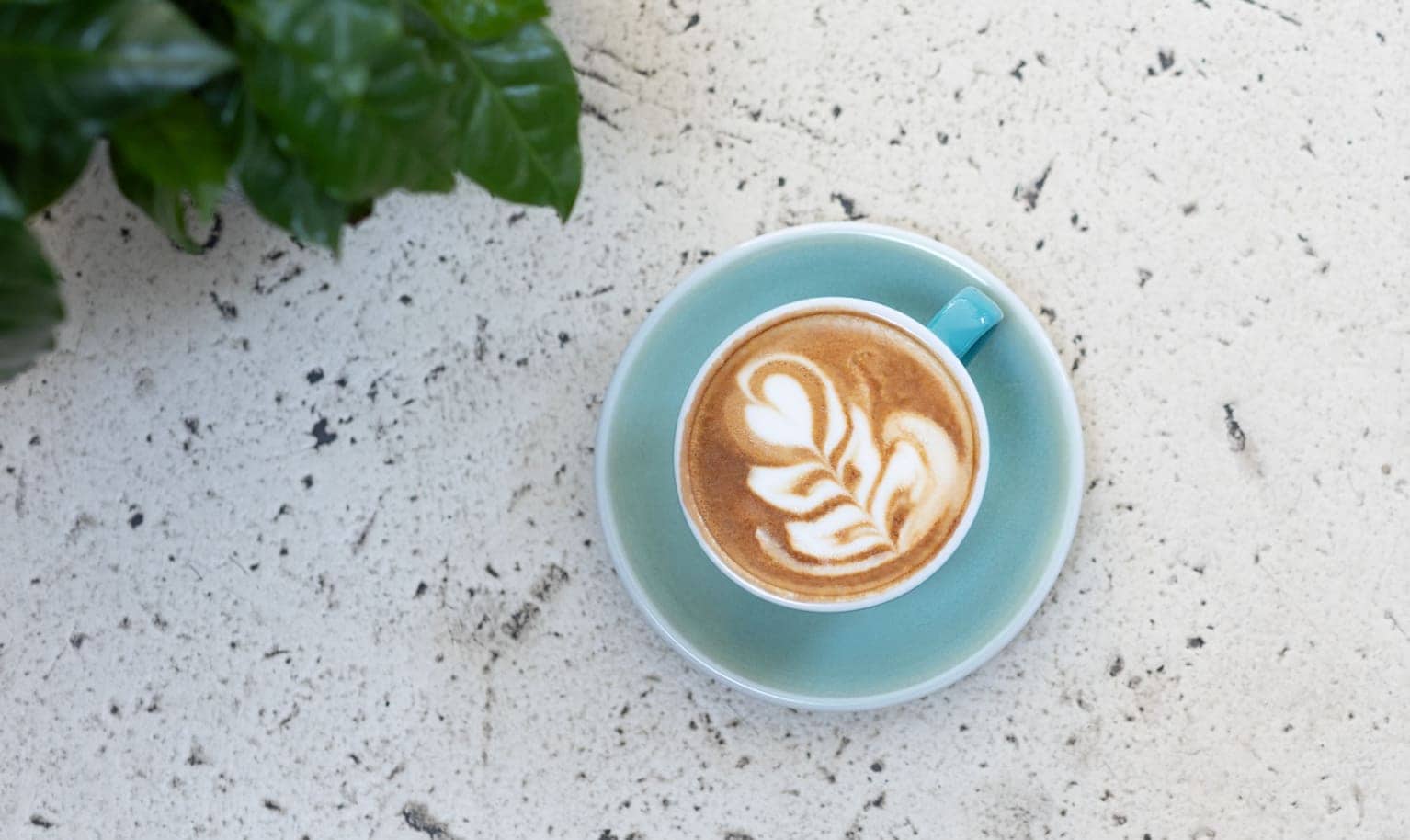 Türkise Cappuccino Tasse steht auf einem Terrazzo Boden.