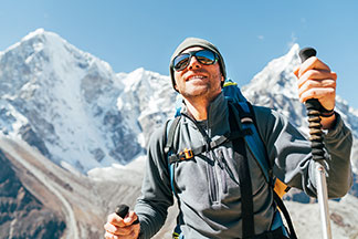 Sportaccessoires für draußen: Ein sportlicher, junger Mann wandert im Hochgebirge mit Wanderstöcken. Dazu trägt er eine Sonnenbrille sowie eine Wollmütze.