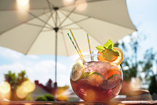 Sichtschutz auf dem Balkon: Auf einem Balkon steht ein sommerlicher Cocktail mit einem weißen Sonnenschirm im Hintergrund.