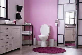 Wohltat für die Füße: Ein violetter, runder Badteppich liegt vor der Toilette in einem modern eingerichteten Bad mit einer rosa Wand.