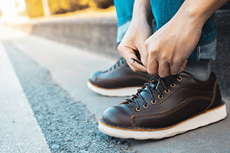 Nahaufnahme von braunen Herren-Halbschuhen, während ein Mann gerade auf einer Treppenstufe sitzt und sich die Schuhe zubindet.