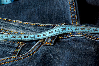 Nahaufnahme einer Jeans und eines Maßbandes entlang des Hosenbundes.