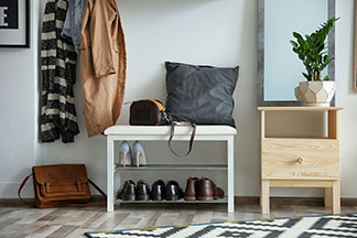 Praktisch und dekorativ: Eine weiße Schuhbank mit Schuhen steht in einem Flur mit einem Spiegel, hängenden Jacken an einer Garderobe und einem Teppich.