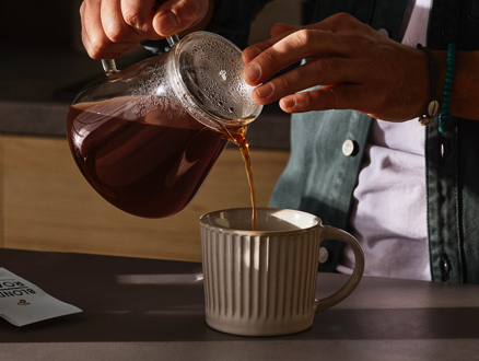 Mann gießt frisch aufgebrühten Filterkaffee aus einer Glaskanne in eine Tasse.
