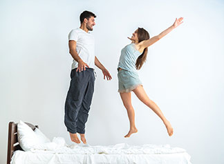Ein Paar springt auf einen Bett in die Luft.