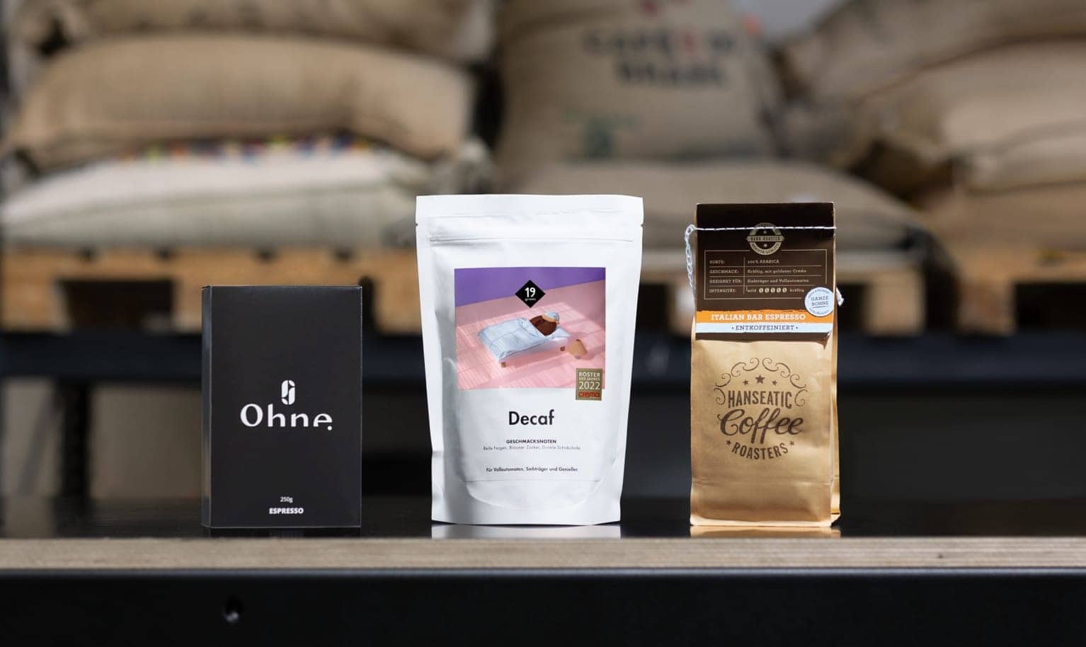 3 Packungen entkoffeinierter Specialty Coffee stehen nebeneinander auf Brett.