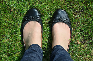 Junge Frau in Jeans und eleganten Sneakern steht angelehnt an einer Wand.