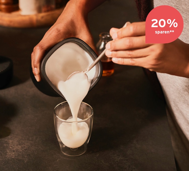 Milchschaum wird aus dem elektrischen Milchaufschäumer in eine Caffè Crema Glas gefüllt.