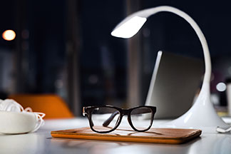 Licht beim Arbeiten: Eine weiße Bürolampe beleuchtet bei Dunkelheit den Schreibtisch.