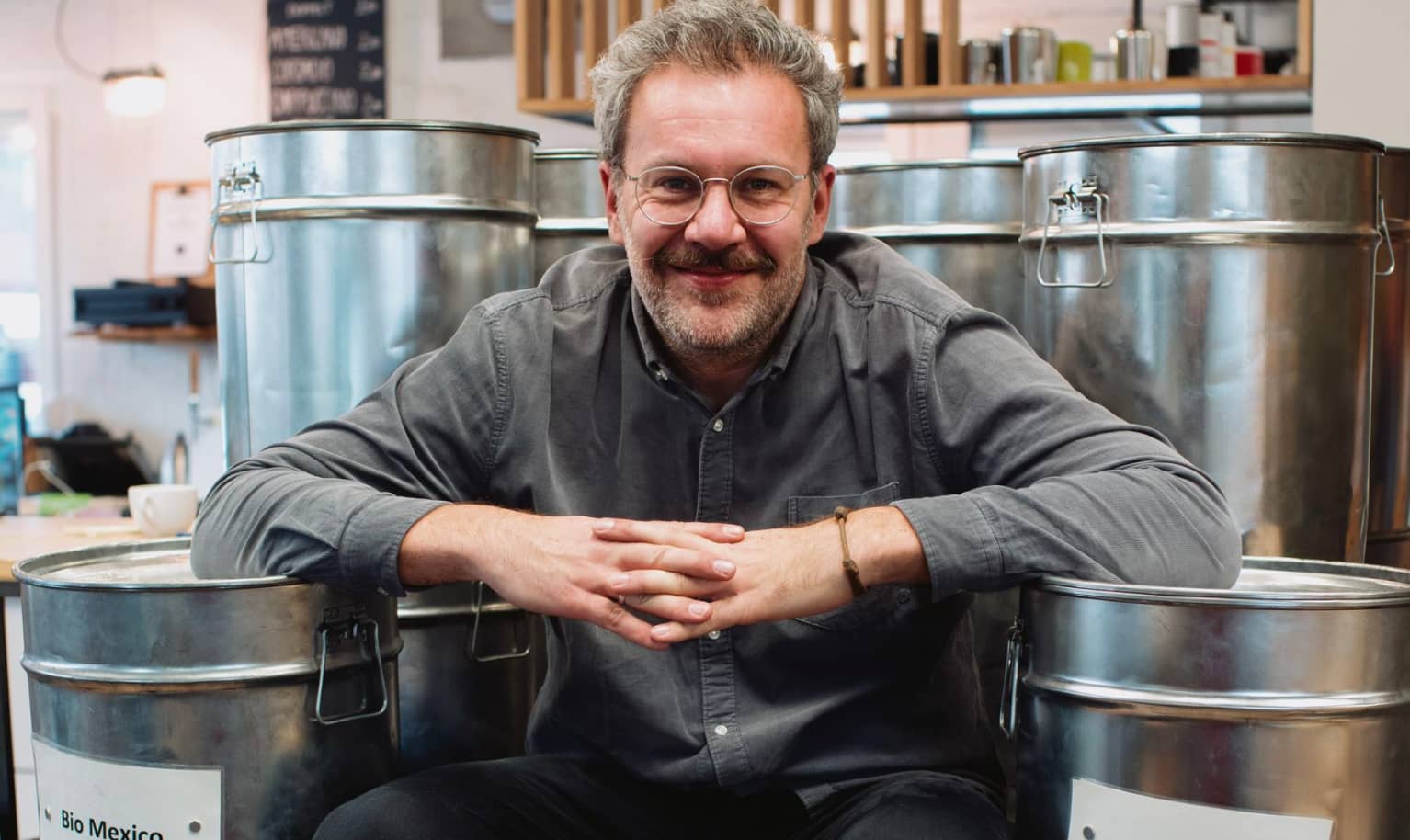 Der Gründer Moritz von der Rösterei Heilandt sitzt lächelnd zwischen Tonnen mit Kaffee
