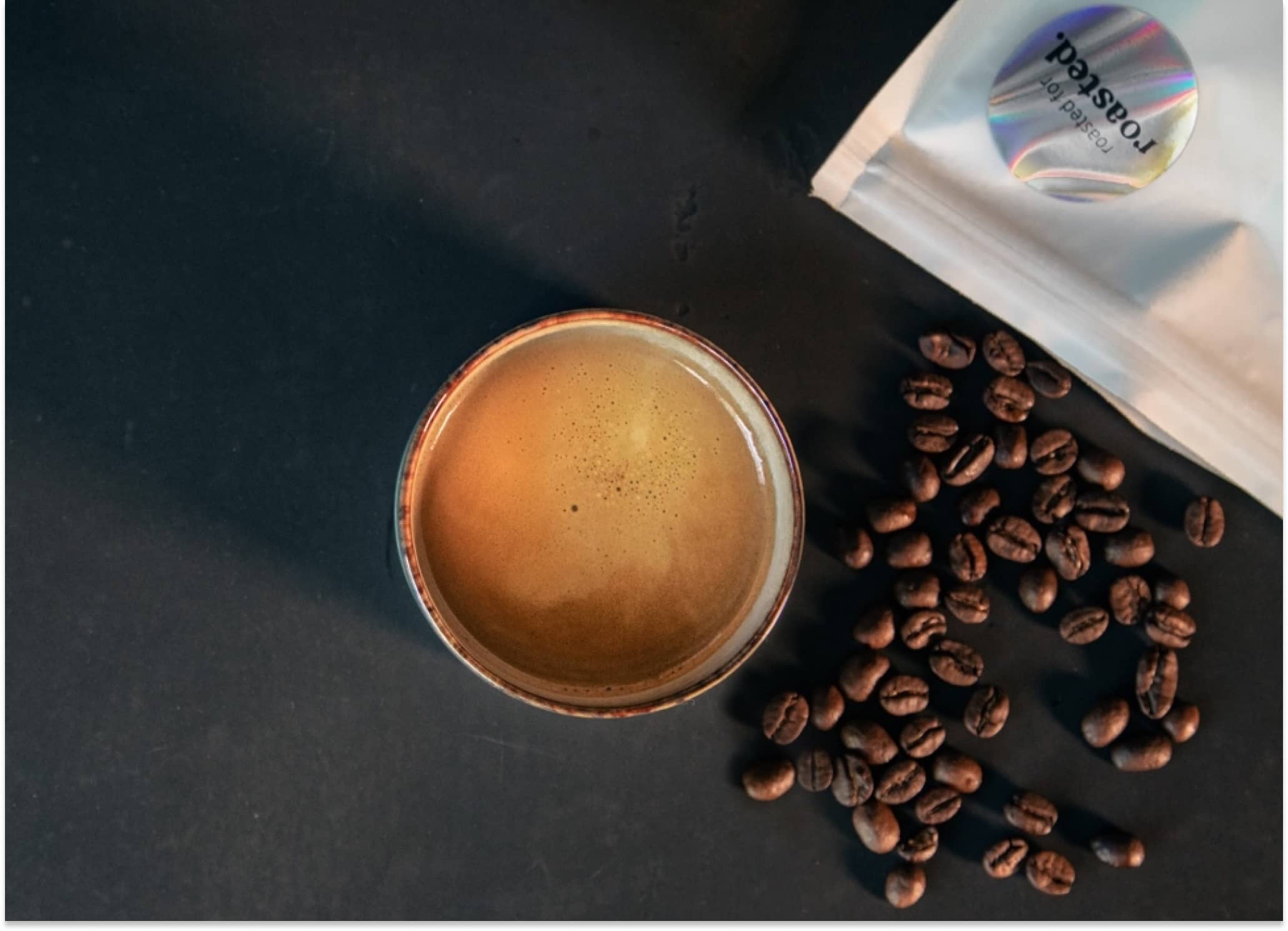 Espressobohnen liegen neben der Co-Roast #1 Verpackungen und einer Espressotasse auf einem Tisch