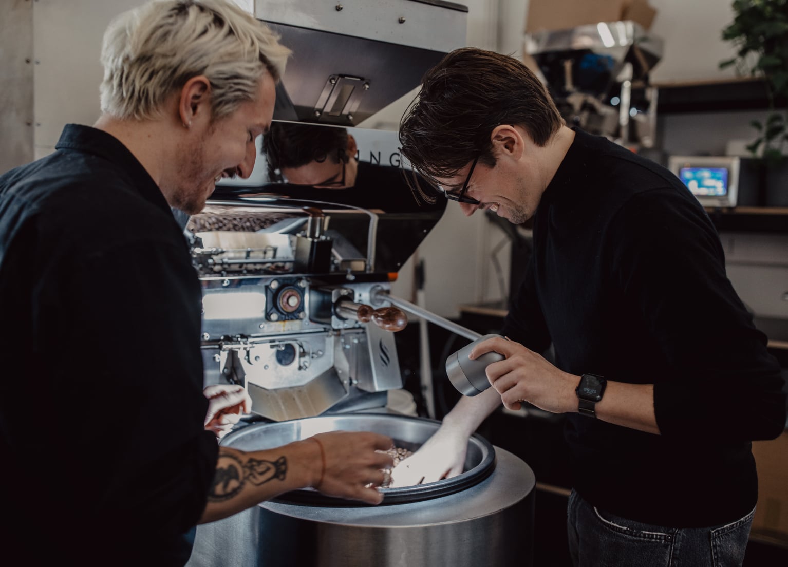 Zwei Mitarbeiter der Rösterei sometime rühren Kaffeebohnen in einer Trommel um