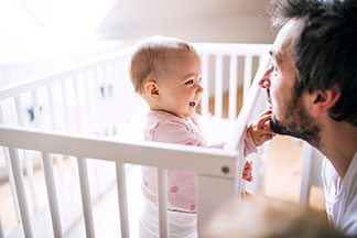 Ein glückliches Baby sitzt im Bett und spielt mit seinem Papa.