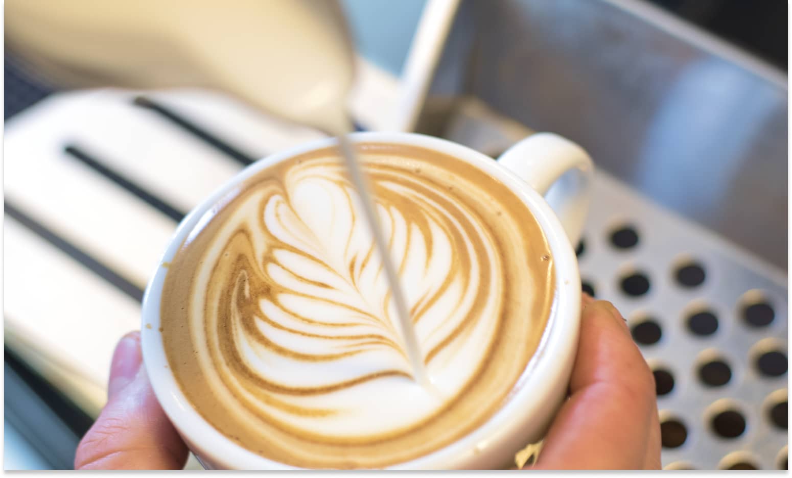 Nahaufnahme wie ein Cappuccino mit Latte Art gegossen wird