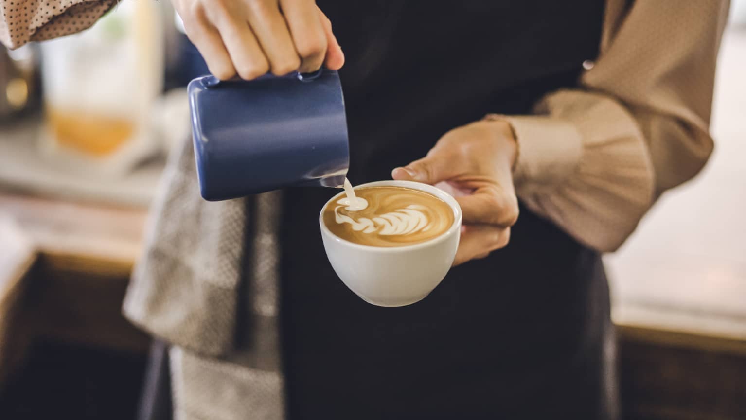 Eine Barista gießt Latte Art in eine Cappuccino Tasse