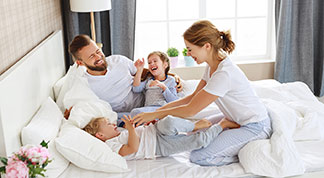 Eine junge Familie – Mutter, Vater, Sohn und Tochter – albert in Nachtwäsche gemeinsam im Bett herum.