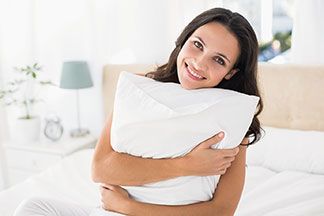 Frau hält lächelnd ein Kopfkissen in der Hand.