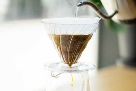 Jemand gießt heißes Wasser in einen Kaffeefilter während der fertige Kaffee unten in die Glaskaraffe läuft