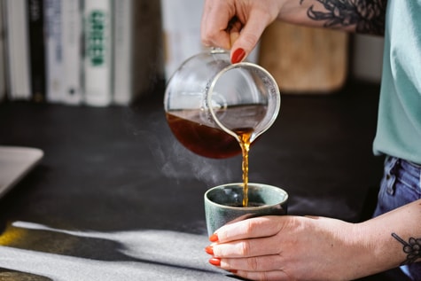 Jemand schenkt sich Filterkaffee aus einer Glaskanne in einen Becher ein.