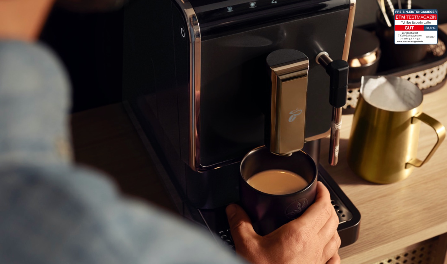 Der Esperto Latte auf einer Küchentheke mit einem frisch aufgebrühten Kaffee und einem goldenen Milchkännchen mit Milchschaum daneben