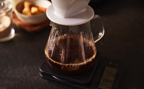 Kaffee läuft durch einen Keramik-Handfilter in eine Glaskanne, die auf einer Kaffeewaage steht