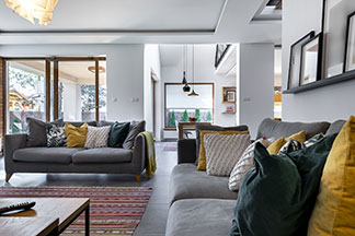 Wohnliche Atmosphäre: Ein großes Wohnzimmer mit einem bunten Teppich und zwei grauen Sofas, die mit vielen bunten Kissen dekoriert sind.