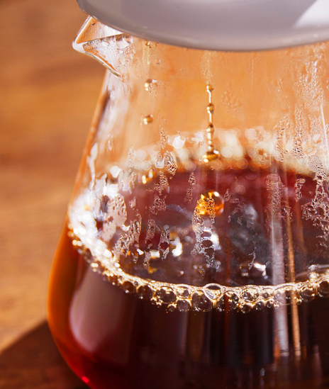 Frisch aufgebrühter Filterkaffee tropft durch einen Kermikhandfilter in eine Glaskanne.