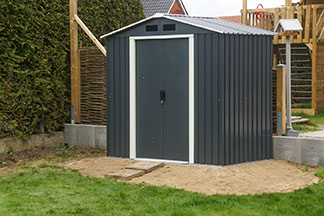 Gartenhaus aus Metall: Ein Gartenhaus, das aus dunklem Material besteht und mit einer weiß eingefassten Tür versehen ist, steht in einem Garten.