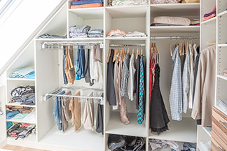 Alles im Blick: Ein begehbarer Schlafzimmerschrank mit vielen verschiedenen offenen Regalen und Fächern in denen Kleidung hängt und liegt.