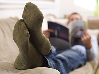 Ein Mann, der grüne Socken trägt, liegt auf seiner Couch und liest eine Zeitschrift.