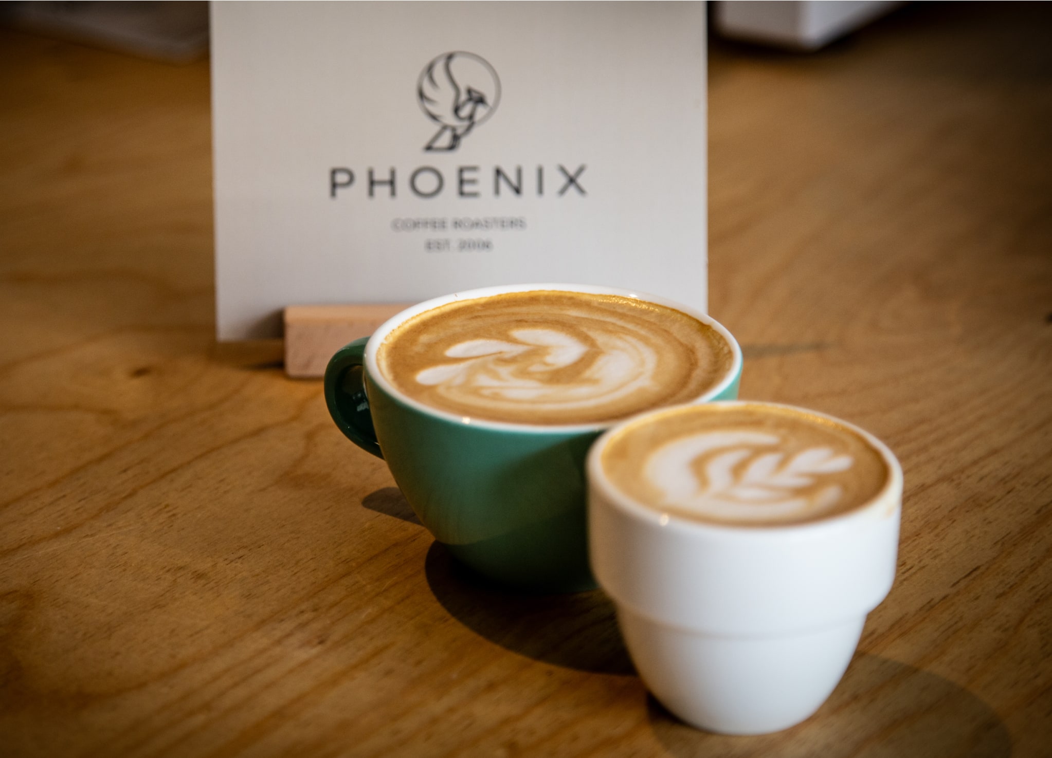 Zwei tassen Cappuccino vor einer Kaffeepackung der Rösterei PHOENIX